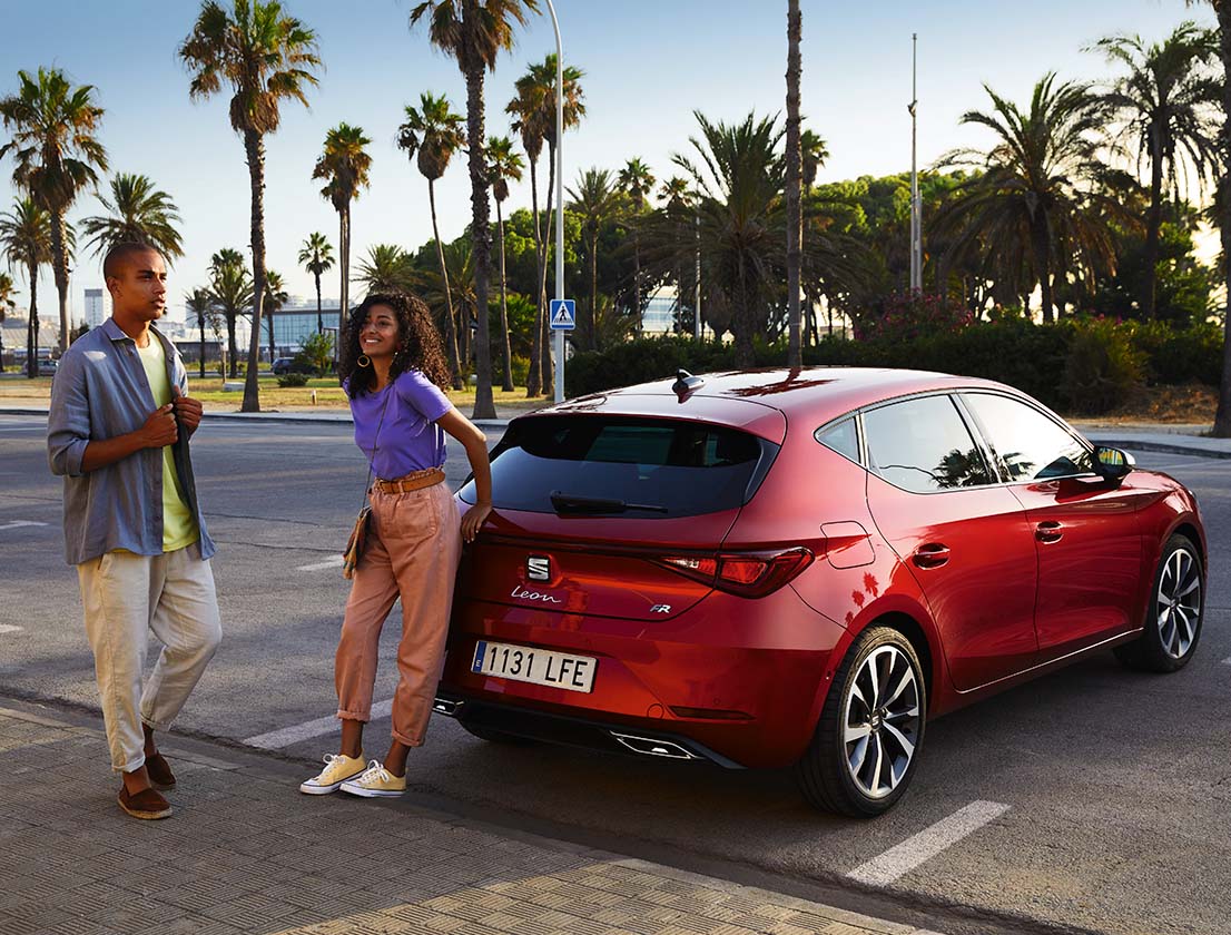 couple talking next to a seat leon desire red colour parked