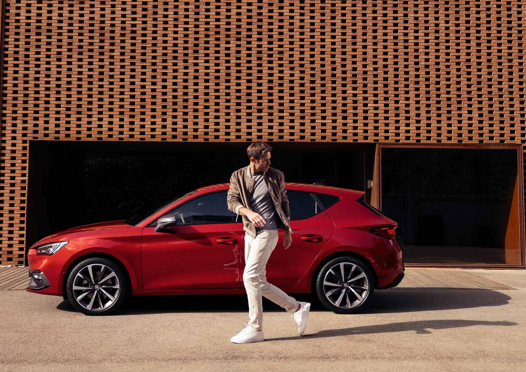 man walking next to seat leon desire red colour with alloy wheels  