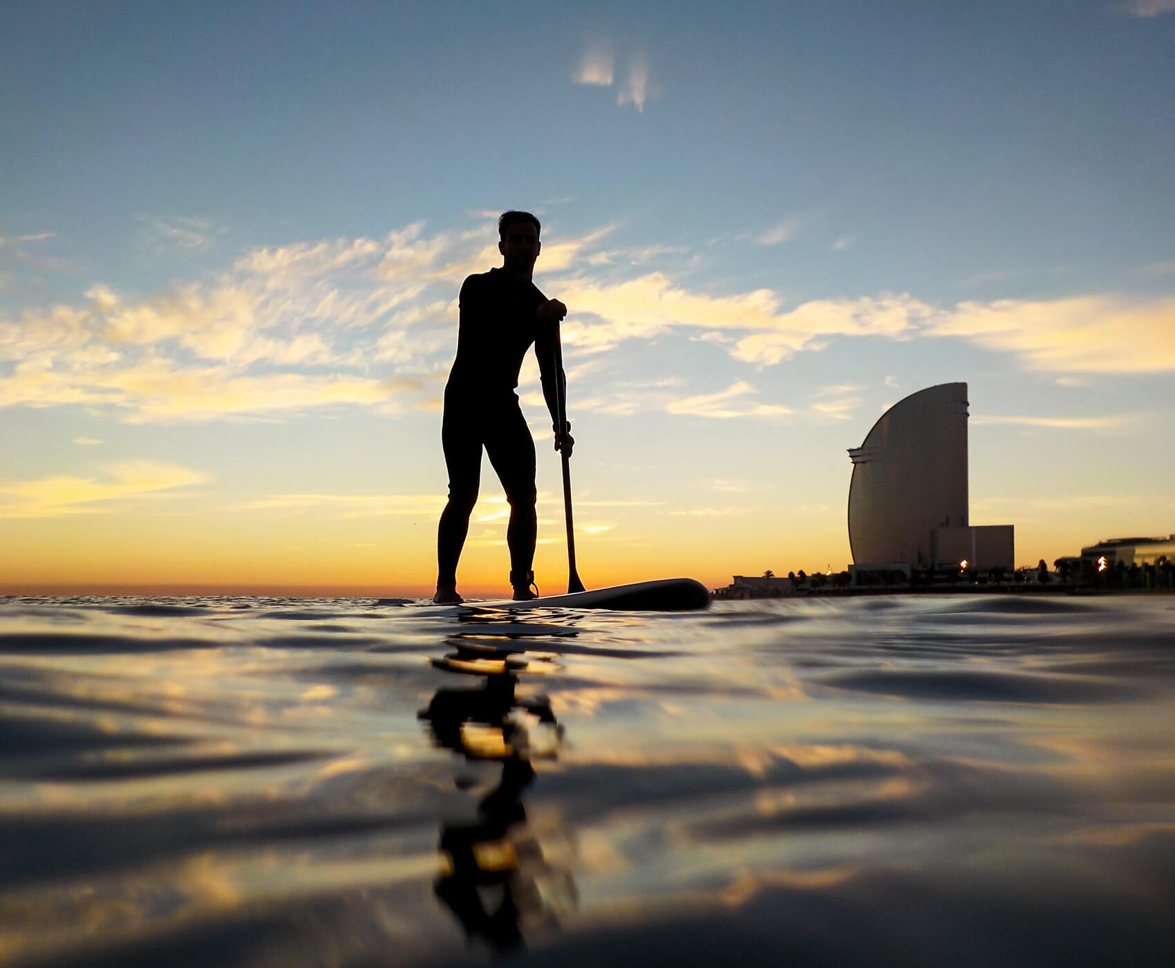 silhouette of a man paddle surfing in Barceloneta beach with the W hotel in the background